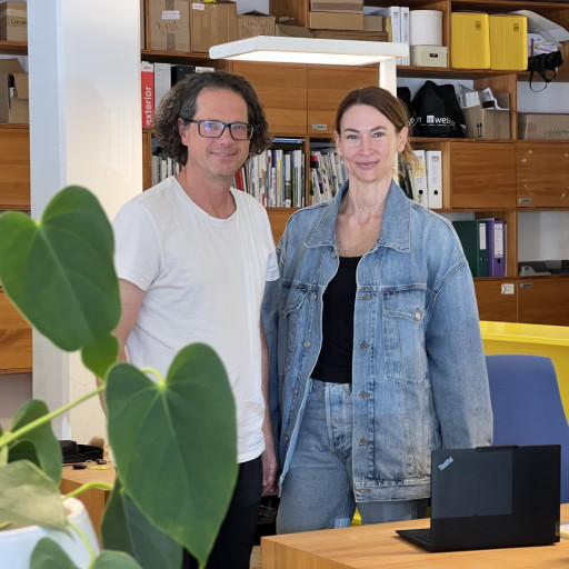 Mann mit Brille und Frau im Jeans-Look stehen in einem Büro mit Holzregalen.