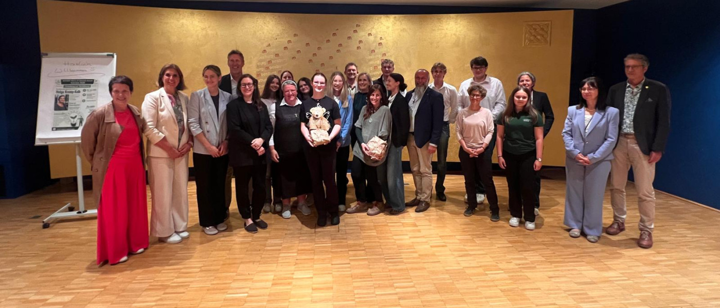 Helga Kump-Gajer mit Gruppe vor Wandbild im Festsaal der Landesberufsschule Zell am See