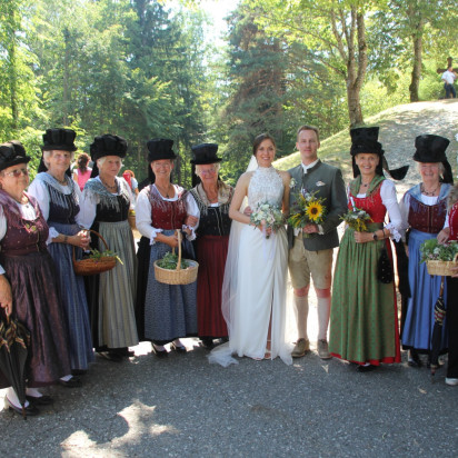 Hochzeitspaar mit Trachtengruppe in Tracht, Brautpaar mit Blumensträußen vor Frauen in traditionellen Trachten