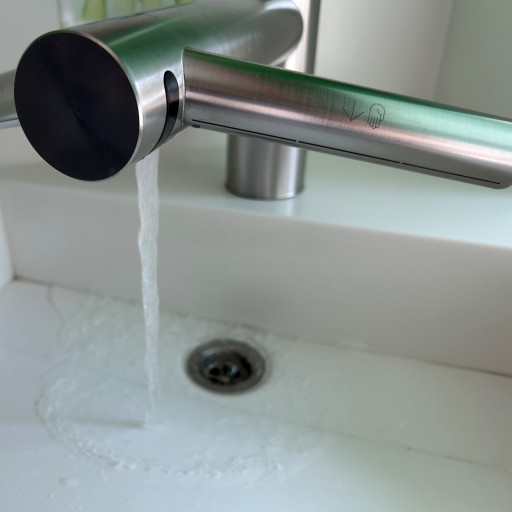 Wasser fließt aus einem Sensorwasserhahn in ein weißes Waschbecken mit einem Abfluss.