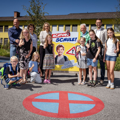 Schulweg-Sicherheit: Kinder und Erwachsene vor Schulschild mit Warnung