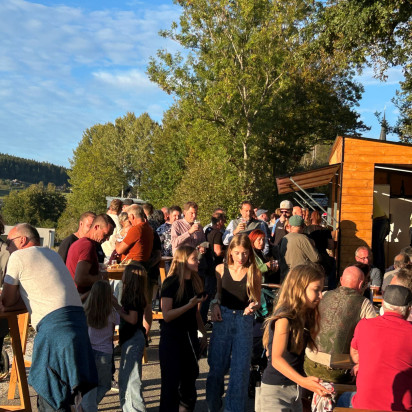 Menschen genießen bei Sonnenschein ein Fest im Freien vor einer Holzhütte.