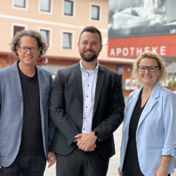 Drei Personen vor einer Apotheke in Österreich: Martin Huber, Bürgermeister von St. Veit, mit zwei Begleitpersonen.